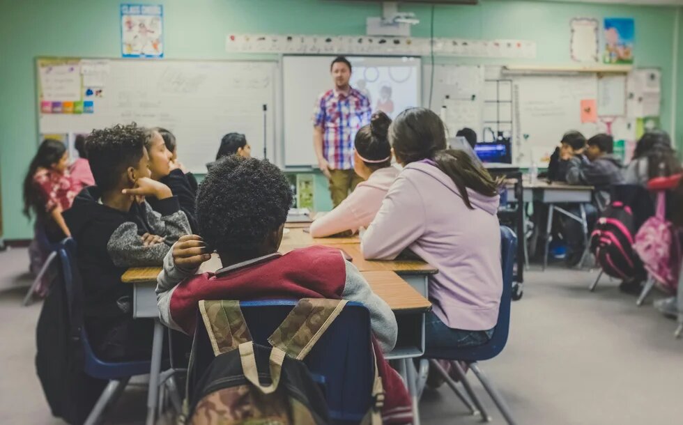 Schüler*innen sitzen in einem Klassenraum und hören der Lehrkraft zu.