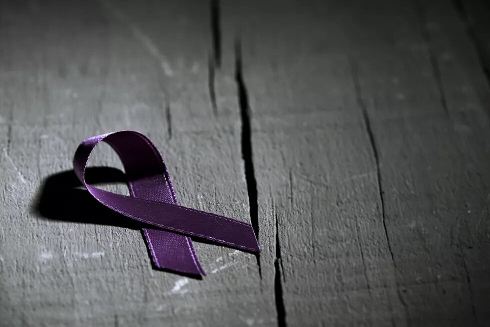 Lila Awareness-Schleife auf dunklem Holz