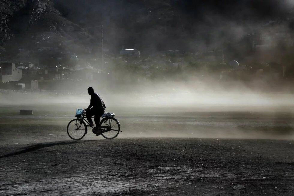 Ein Mann mit einem Fahrrad fährt vor einer in Nebel oder Gas verhangenen Stadt