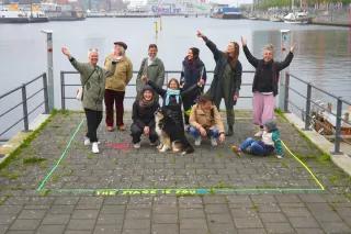 KunstMacht und Cultural Planning Workshop Visionsentwicklung Acht Erwachsene, ein Kind und ein Hund posieren in einem Rechteck vor der Ostsee.