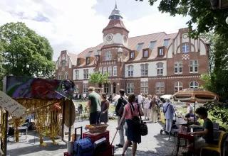 Vor dem Corworkhaus im Anscharpark Kiel stehen Flohmarktstände. Viele Menschen laufen umher.